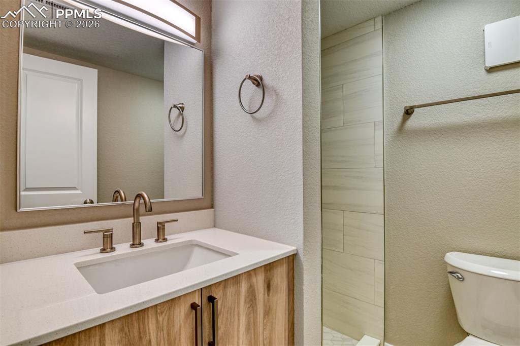 Bathroom featuring a textured wall, vanity, and tiled shower