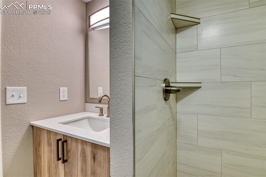 Bathroom with a textured wall, vanity, and a tile shower