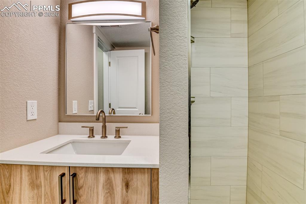 Full bathroom featuring a textured wall, vanity, and tiled shower