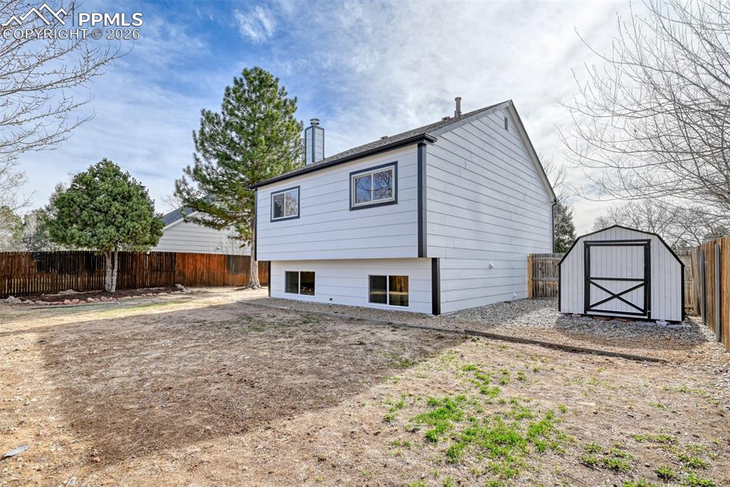 Back of house with a fenced backyard, a storage shed, and a chimney