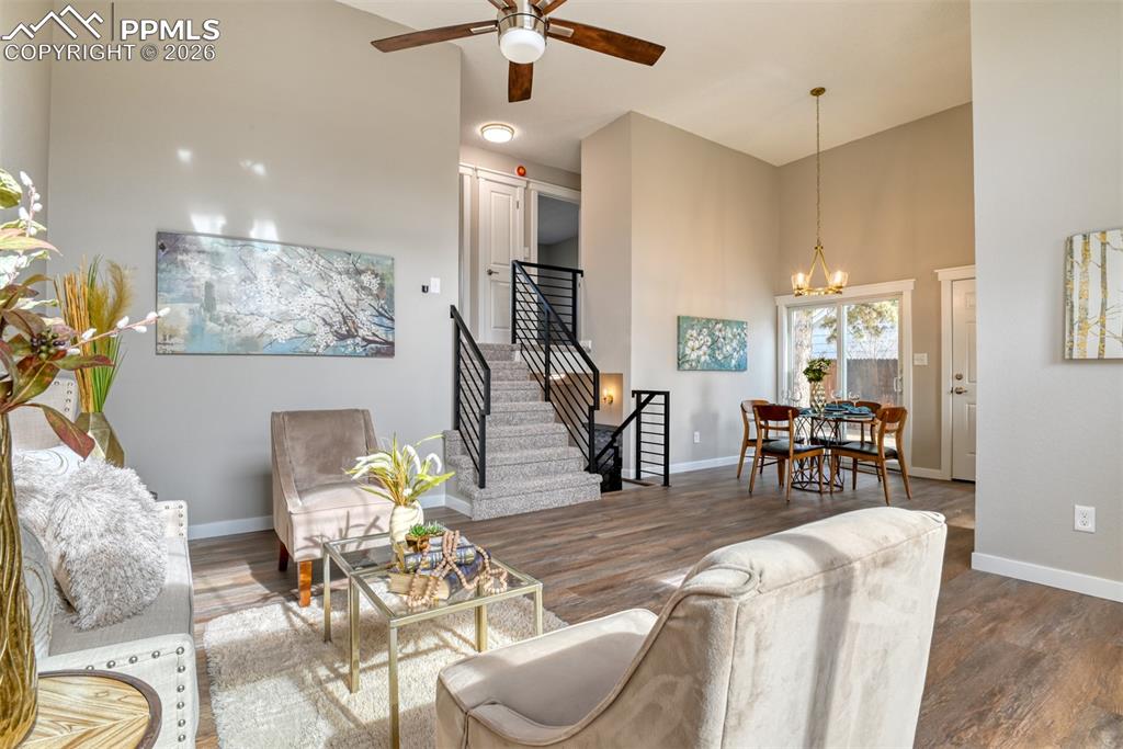 Living area with a high ceiling, a ceiling fan, wood finished floors, and suspended lighting