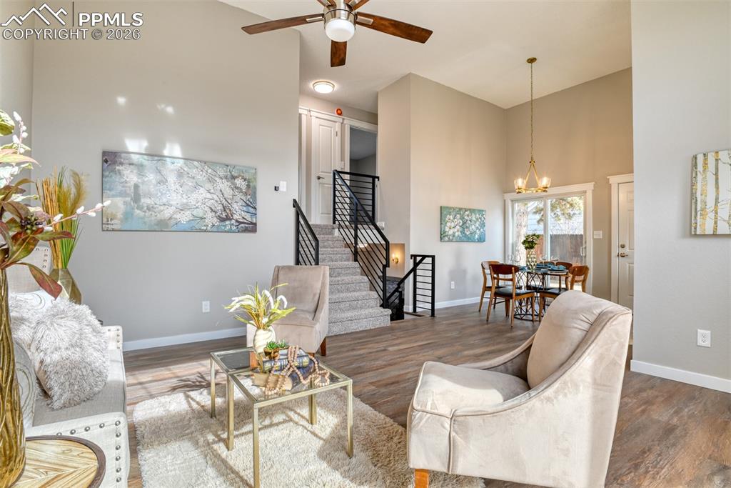 Living area with a high ceiling, wood finished floors, ceiling fan, and a chandelier