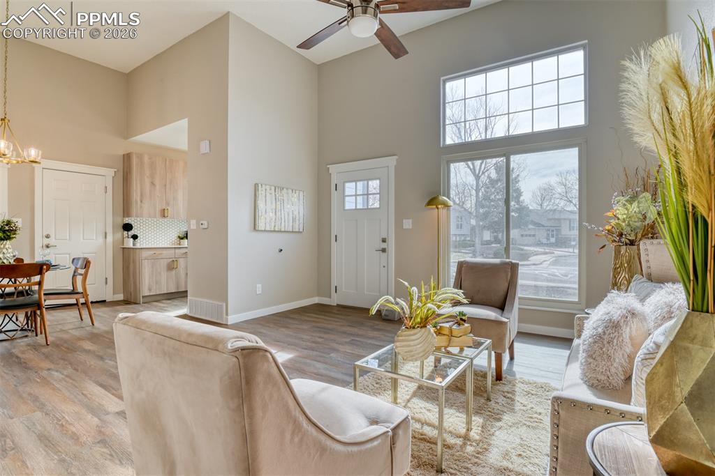 Living room featuring a high ceiling, light wood-style flooring, a ceiling fan, and suspended lighting