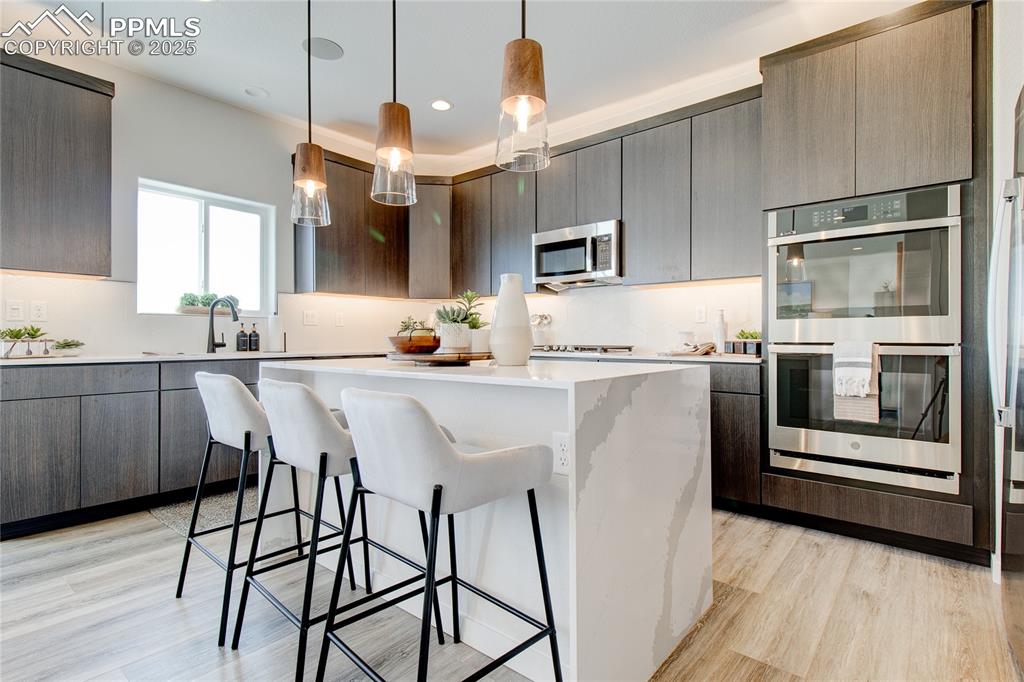 Kitchen featuring a kitchen breakfast bar, stainless steel appliances, hanging light fixtures, light wood-type flooring, and a kitchen island