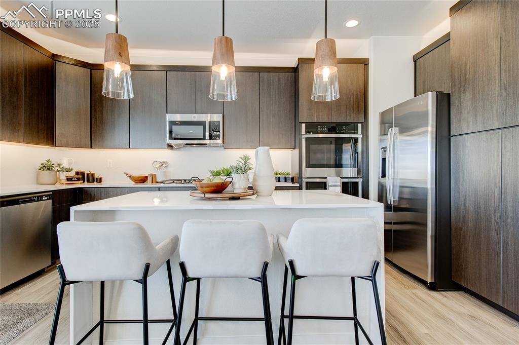 Kitchen with a kitchen breakfast bar, appliances with stainless steel finishes, pendant lighting, light wood-type flooring, and recessed lighting