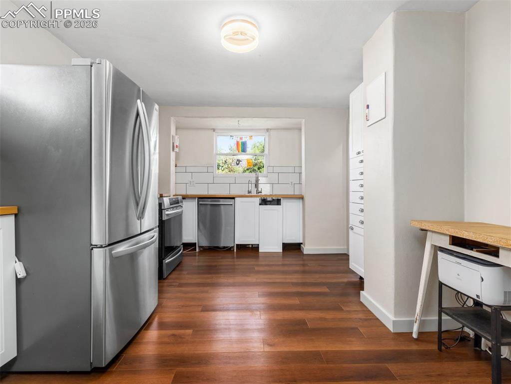 Kitchen with stainless steel appliances, white cabinets, dark wood finished floors, decorative backsplash, and butcher block countertops