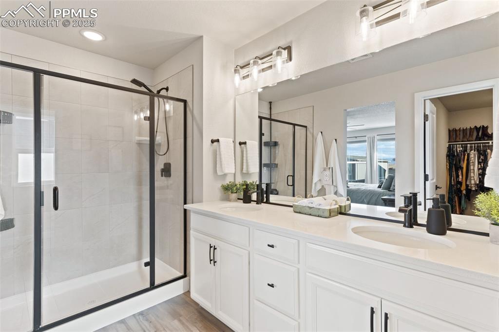 Ensuite bathroom featuring a stall shower, double vanity, light wood-type flooring, a spacious closet, and recessed lighting