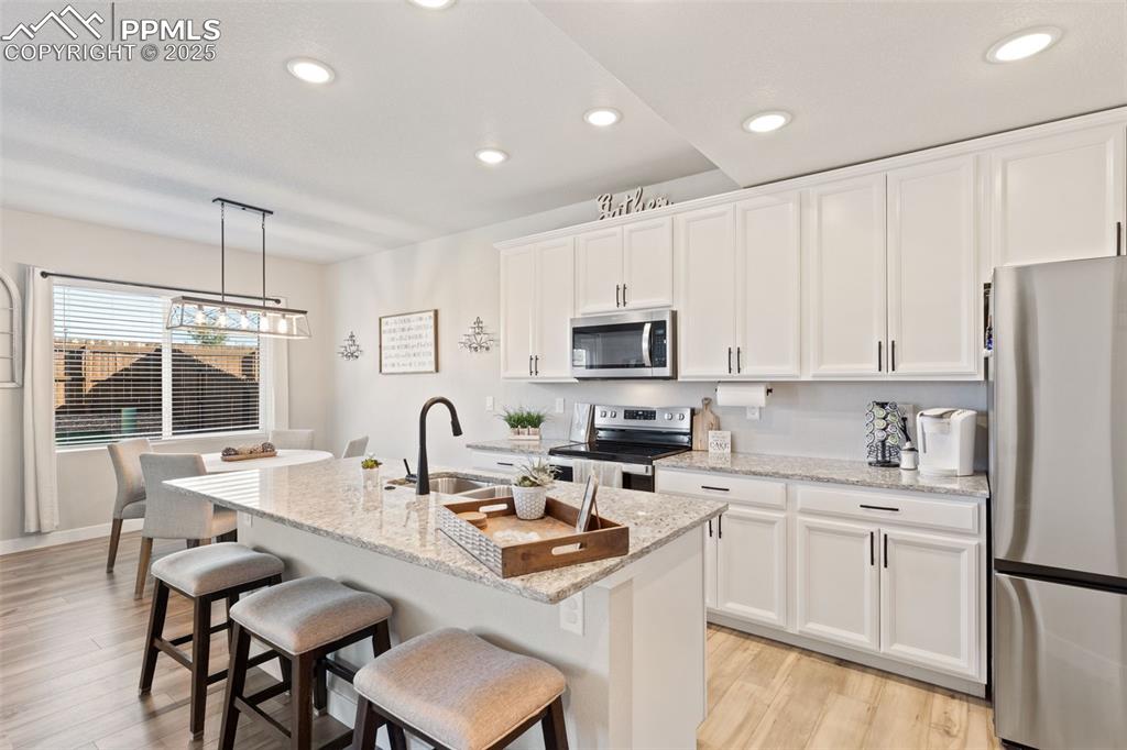 Kitchen featuring stainless steel appliances, decorative light fixtures, white cabinets, light stone counters, and recessed lighting