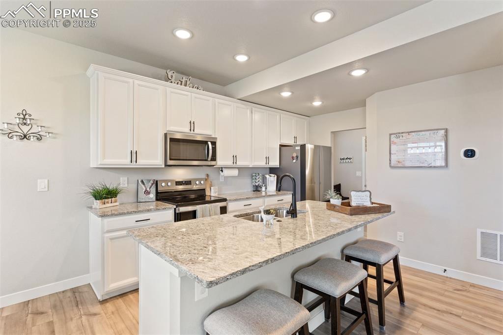 Kitchen with stainless steel appliances, a kitchen bar, white cabinetry, light stone counters, and recessed lighting