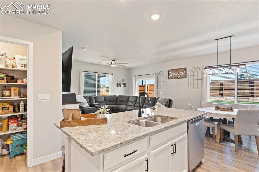 Kitchen featuring white cabinets, light wood finished floors, light stone countertops, a kitchen island with sink, and open floor plan