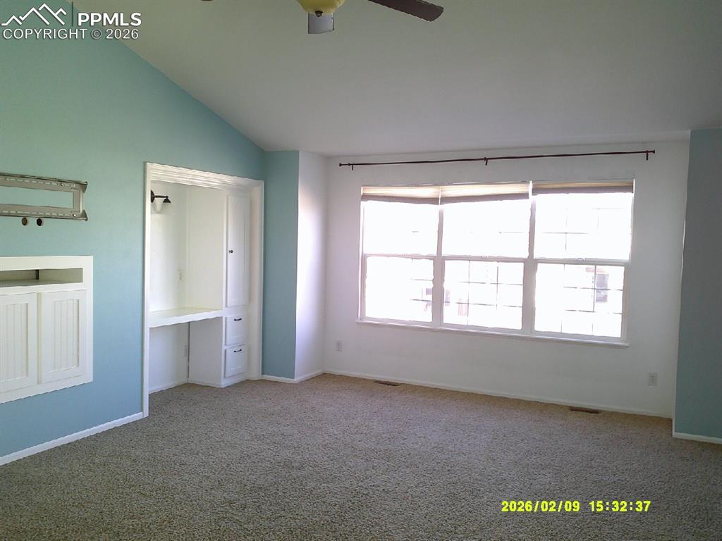 Unfurnished bedroom featuring carpet flooring, a ceiling fan, lofted ceiling, and a desk