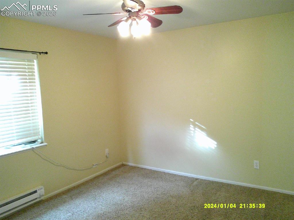 Empty room featuring a baseboard radiator, ceiling fan, and carpet flooring