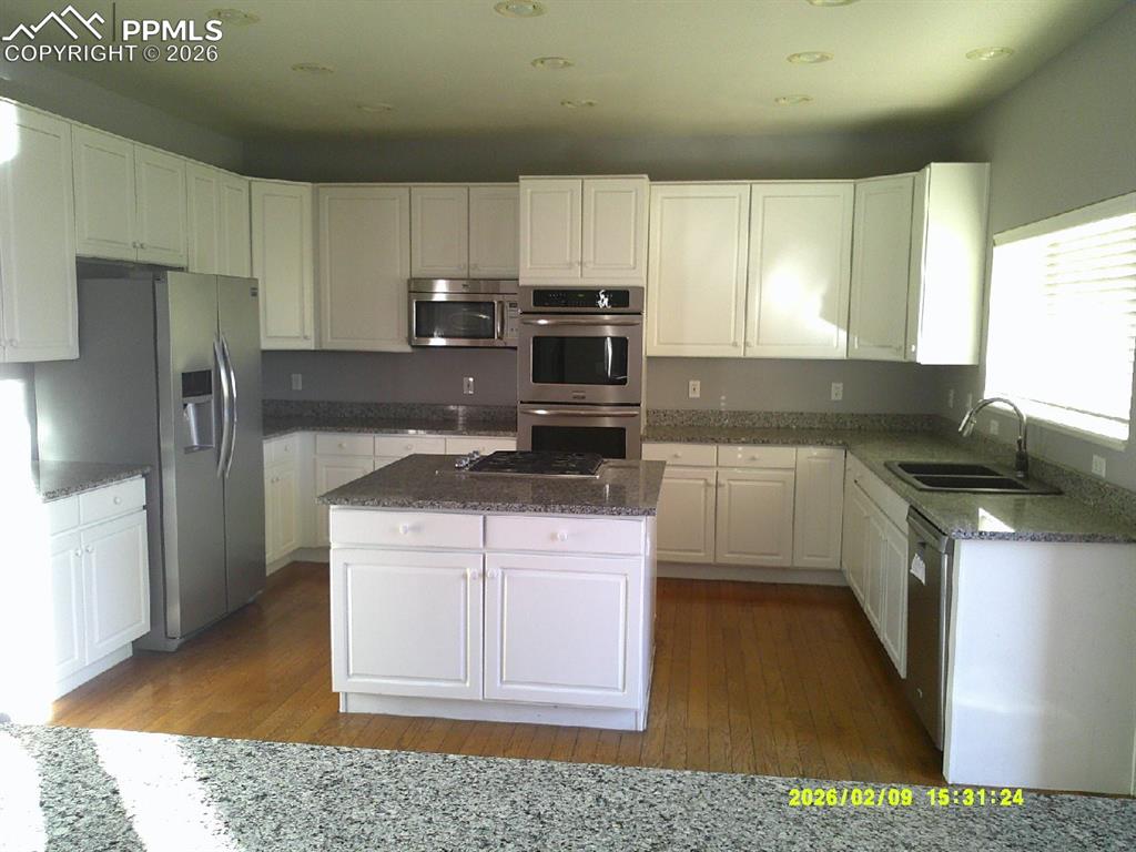 Kitchen featuring white cabinetry, dark stone countertops, stainless steel appliances, and dark wood-type flooring