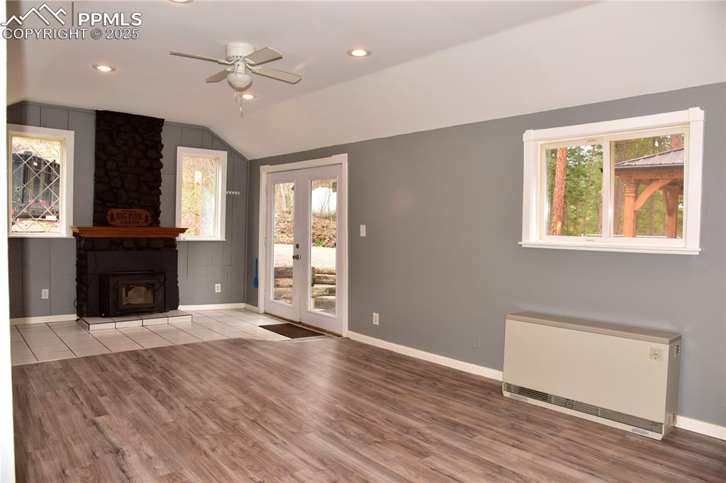 Unfurnished living room with radiator, ceiling fan, vaulted ceiling, wood finished floors, and baseboards