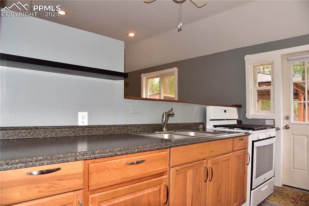 Kitchen with white gas range oven, a sink, healthy amount of natural light, dark countertops, and recessed lighting
