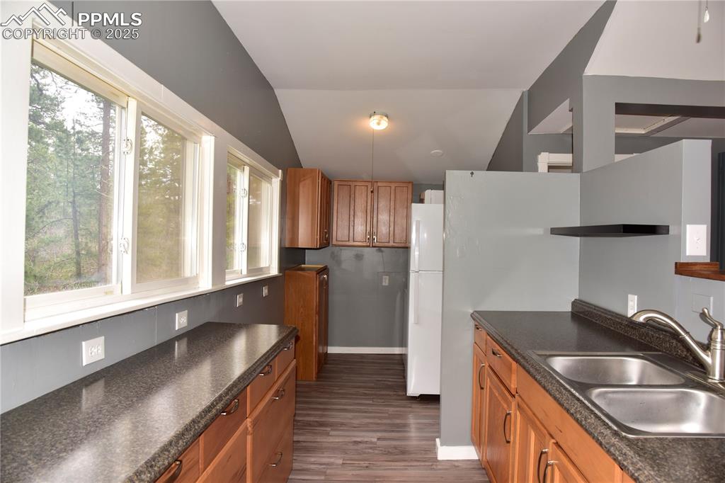 Kitchen featuring a sink, freestanding refrigerator, dark countertops, dark wood-type flooring, and lofted ceiling