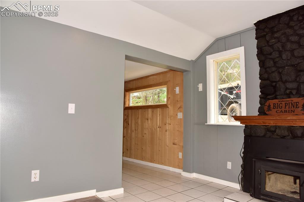 Unfurnished living room with baseboards, vaulted ceiling, light tile patterned floors, wood walls, and a glass covered fireplace