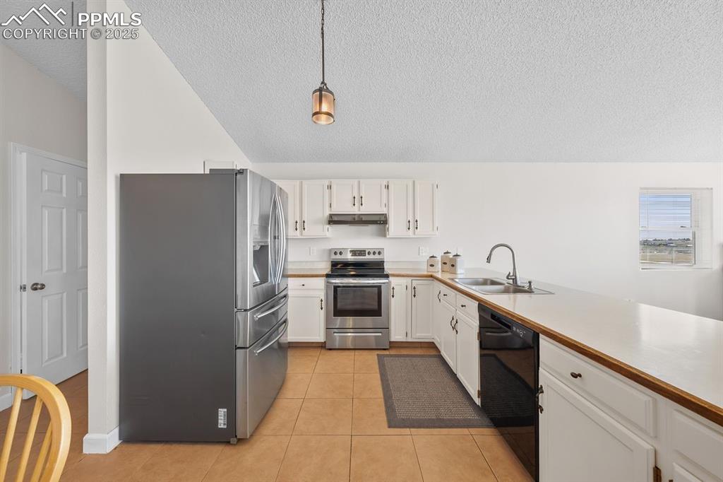 Kitchen featuring appliances with stainless steel finishes, light countertops, light tile floors and white cabinetry