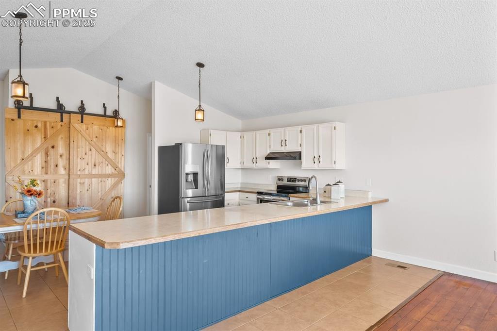 Kitchen featuring light countertops, stainless steel appliances, large counter space, vaulted ceiling, and hanging light pendants