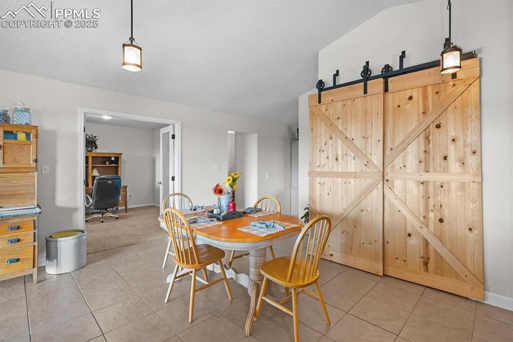 Dining space with tile floors, a barn door, and vaulted ceiling