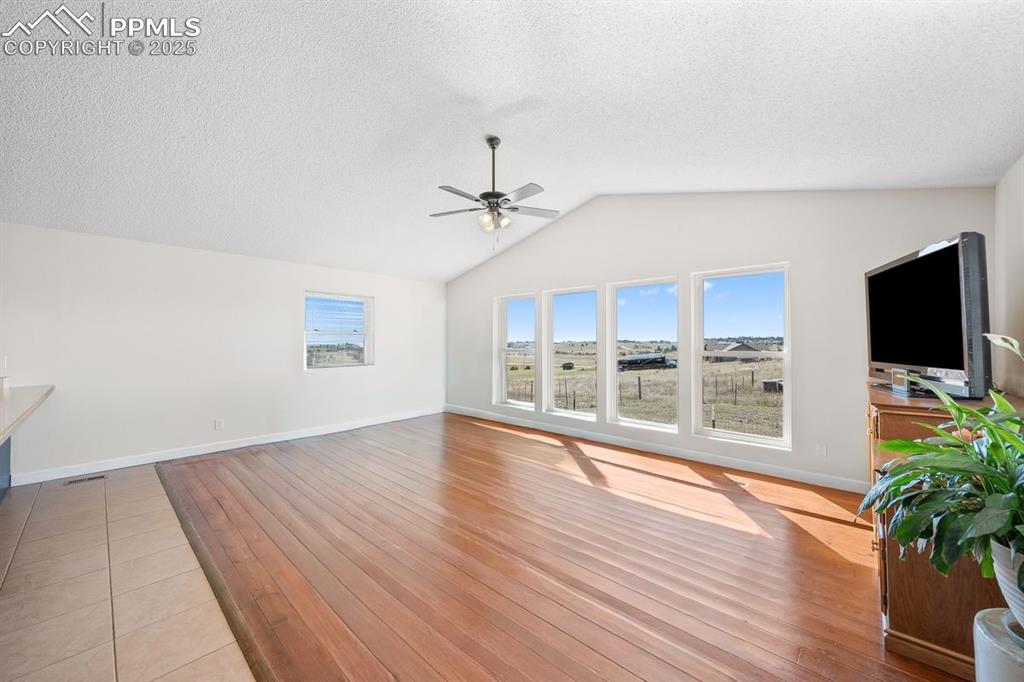 Unfurnished living room with plenty of natural light, vaulted ceiling, wood flooring and ceiling fan