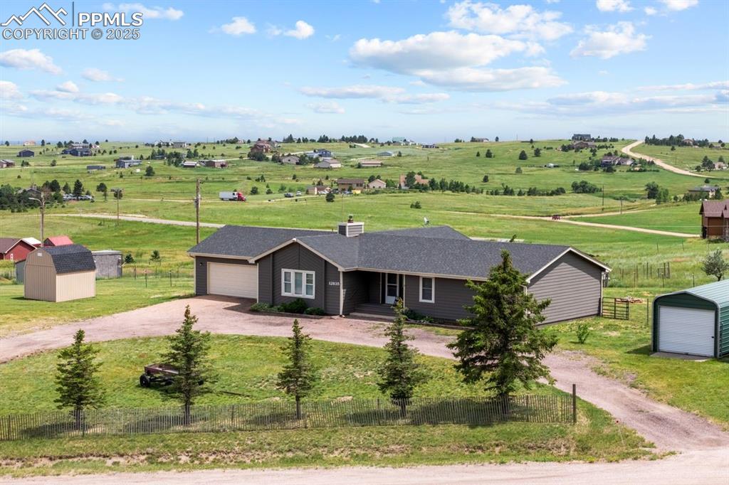 View of front of home with a view of countryside, dirt circular driveway and storage sheds 