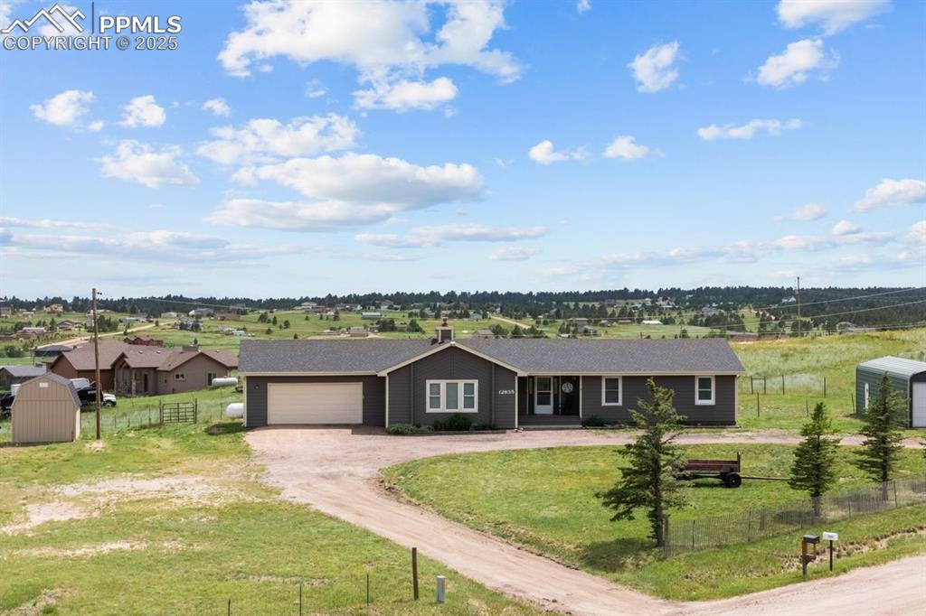 Ranch-style house featuring dirt driveway, two storage shed, a detached garage, a view of rural / pastoral area, and covered porch