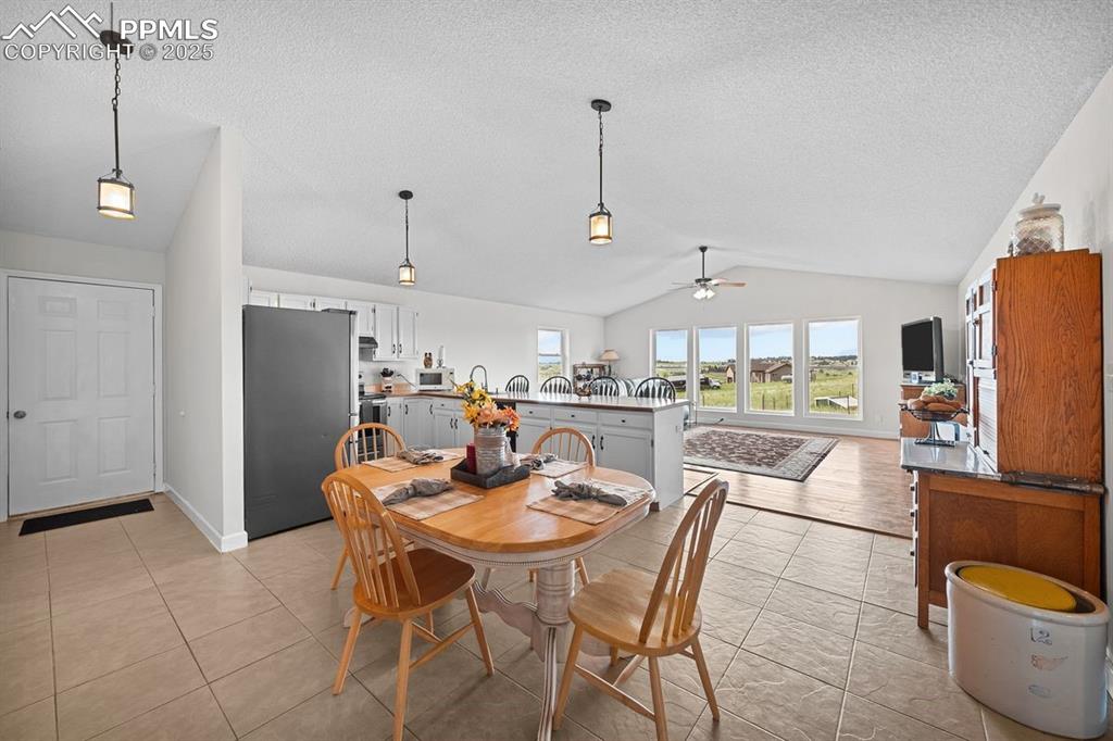 Dining space featuring vaulted ceiling, a ceiling fan and tile floors