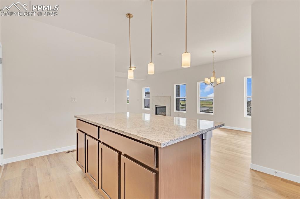Kitchen with a tiled fireplace, decorative light fixtures, light stone countertops, and light wood finished floors