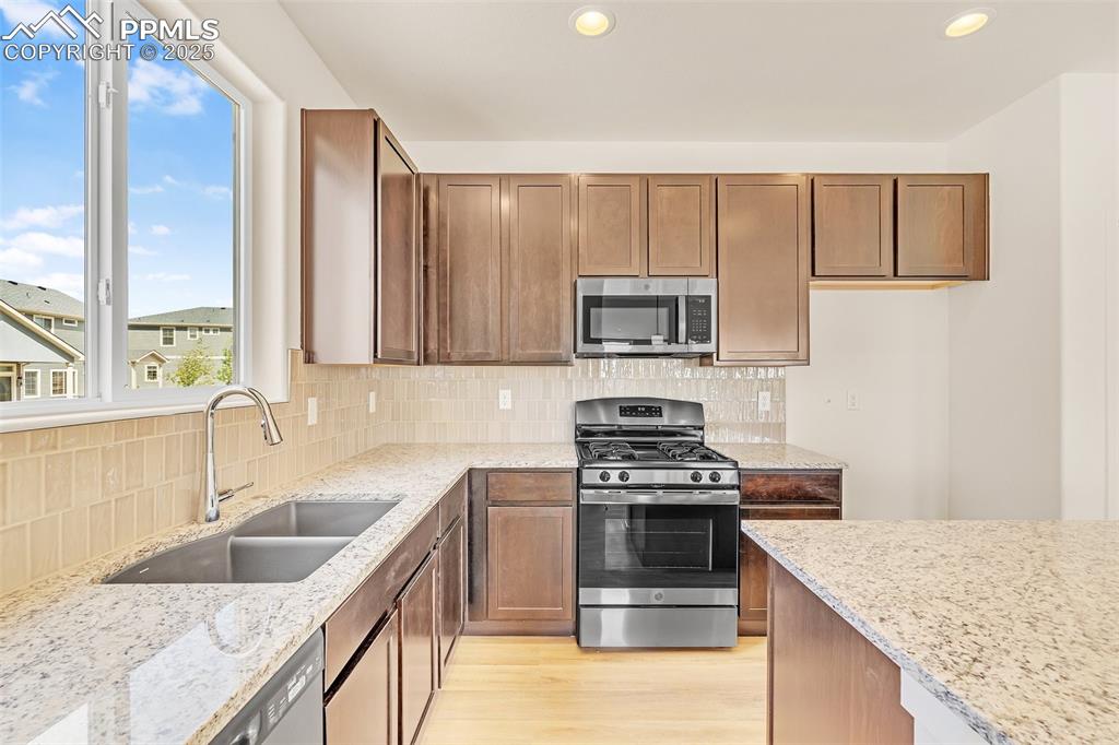 Kitchen featuring appliances with stainless steel finishes, tasteful backsplash, light stone counters, recessed lighting, and brown cabinets