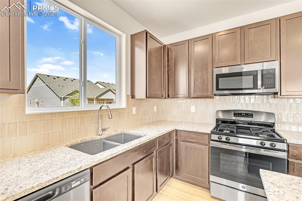 Kitchen with appliances with stainless steel finishes, tasteful backsplash, and light stone countertops