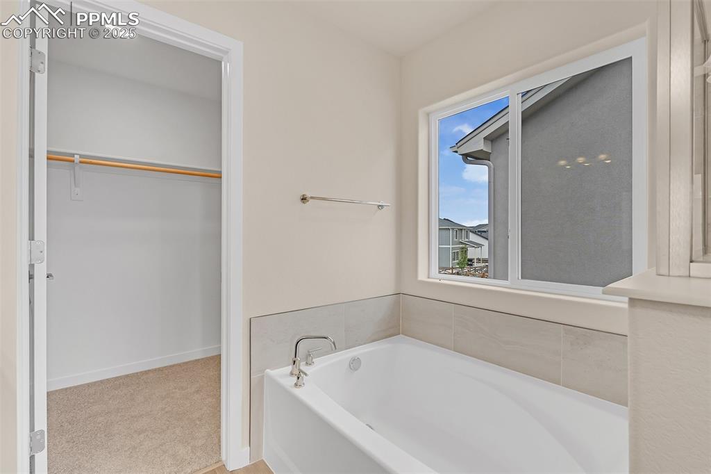 Full bath with a garden tub, a walk in closet, and light carpet