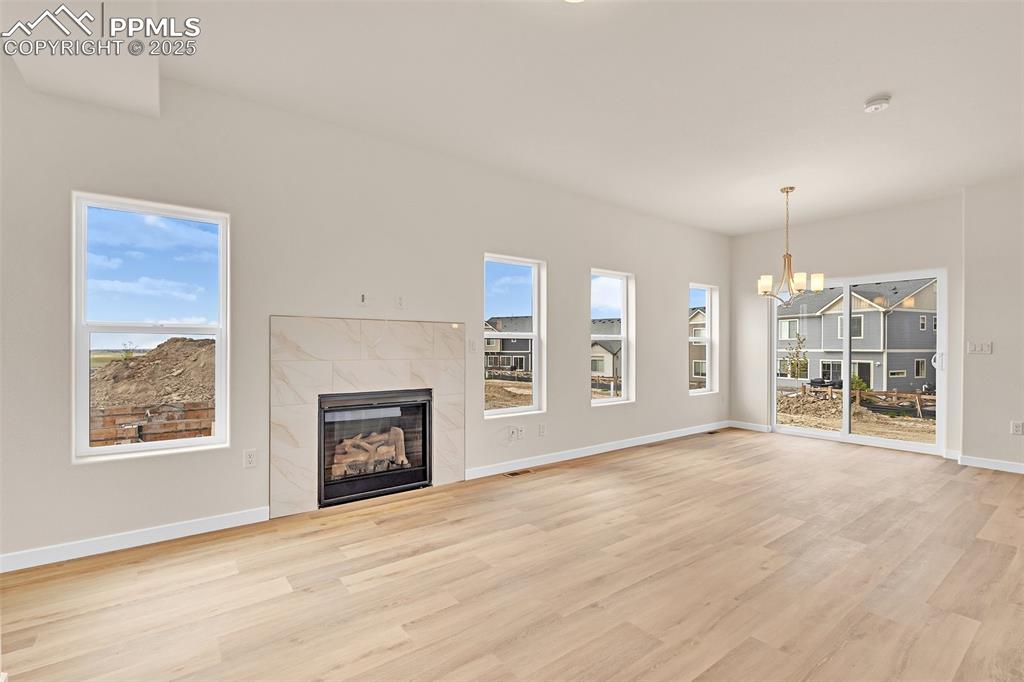 Unfurnished living room with a fireplace, a chandelier, light wood-style flooring, and healthy amount of natural light