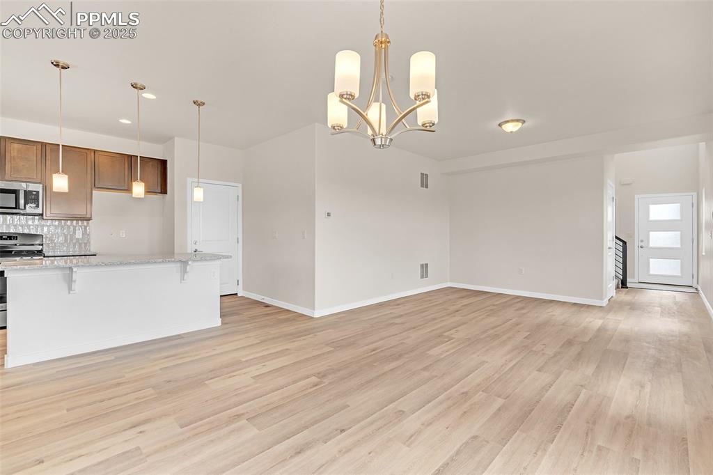 Kitchen featuring a kitchen breakfast bar, pendant lighting, light stone counters, appliances with stainless steel finishes, and backsplash
