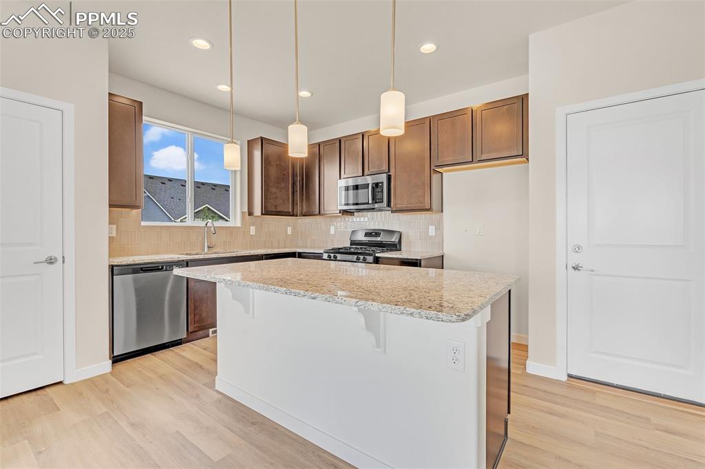 Kitchen with a breakfast bar area, tasteful backsplash, pendant lighting, light stone countertops, and recessed lighting