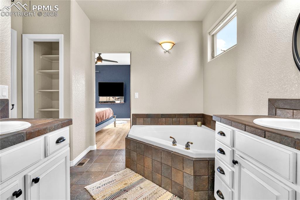 Bathroom with two vanities, a garden tub, a textured wall, a ceiling fan, and connected bathroom