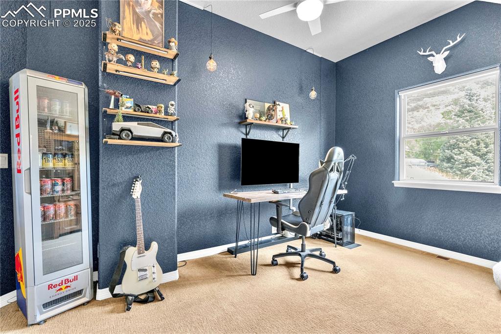 Carpeted office featuring a textured wall and ceiling fan