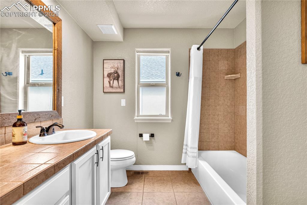 Full bath with vanity, a textured wall, a textured ceiling, shower / tub combo, and tile patterned floors