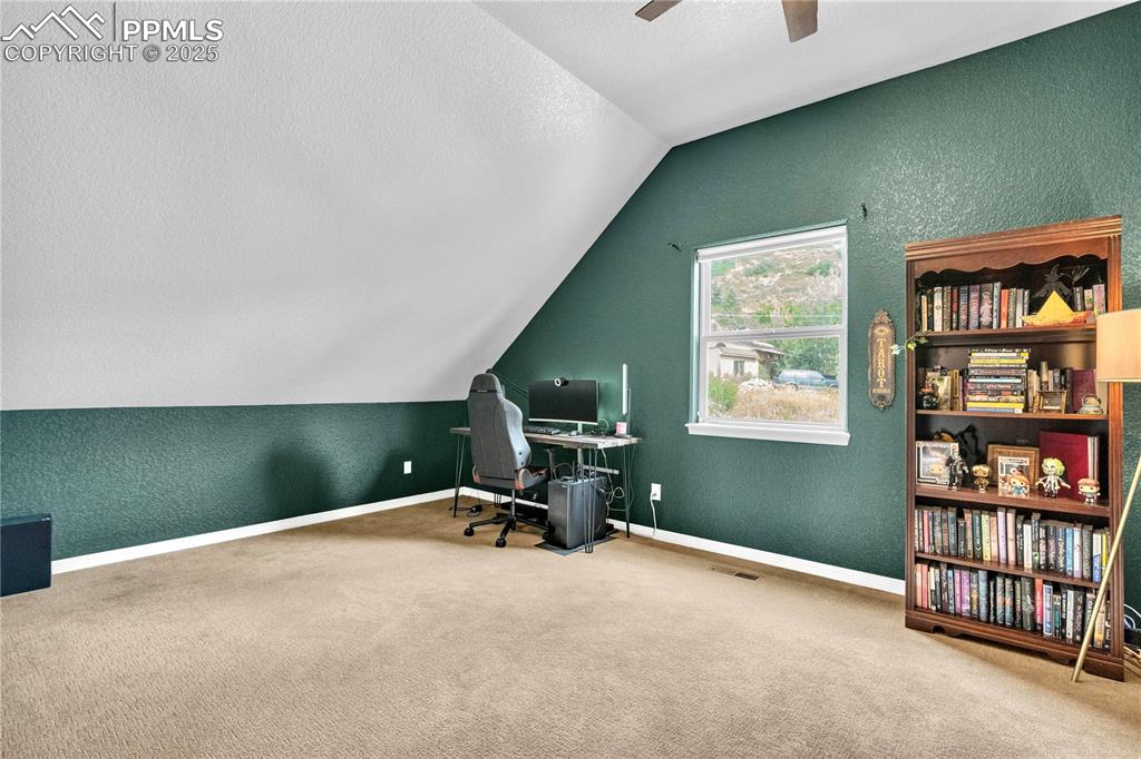 Carpeted office space featuring a textured wall, a textured ceiling, lofted ceiling, and a ceiling fan