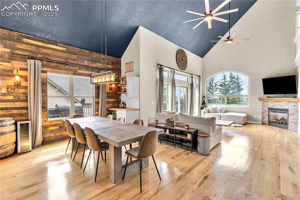Dining space with light wood-type flooring, wood walls, a fireplace, high vaulted ceiling, and a textured ceiling