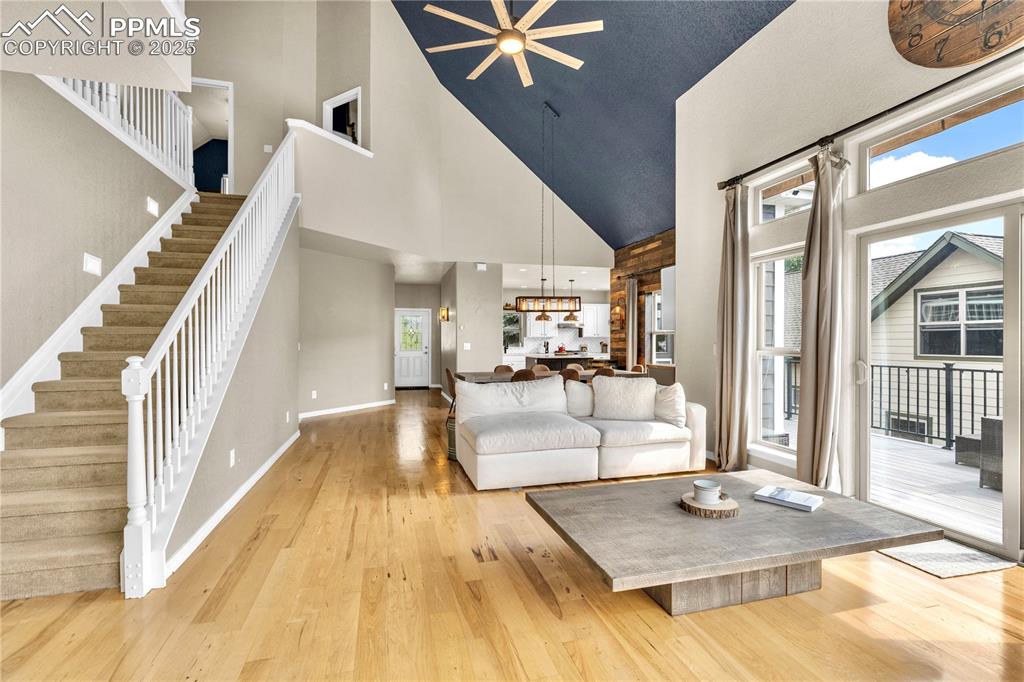 Living area featuring light wood-type flooring, ceiling fan, high vaulted ceiling, and stairs