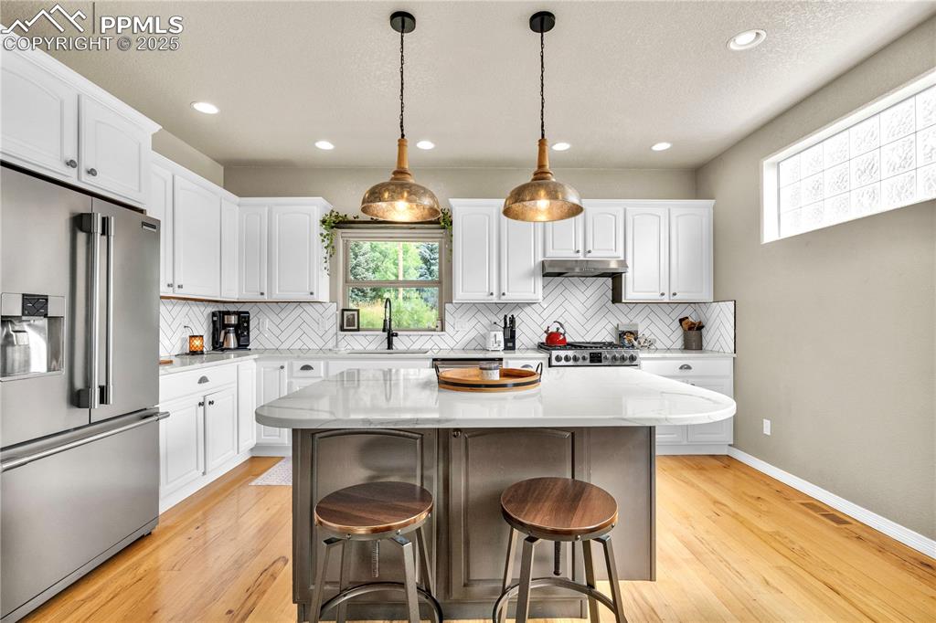 Kitchen with high quality fridge, light wood-style flooring, a breakfast bar area, white cabinetry, and recessed lighting