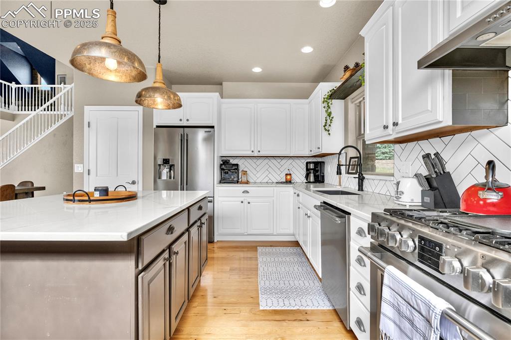 Kitchen featuring appliances with stainless steel finishes, light wood-style floors, tasteful backsplash, white cabinets, and under cabinet range hood
