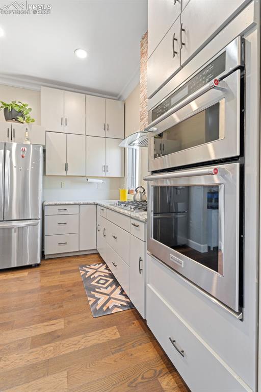 Kitchen with appliances with stainless steel finishes, light wood-style floors, light stone counters, white cabinets, and recessed lighting