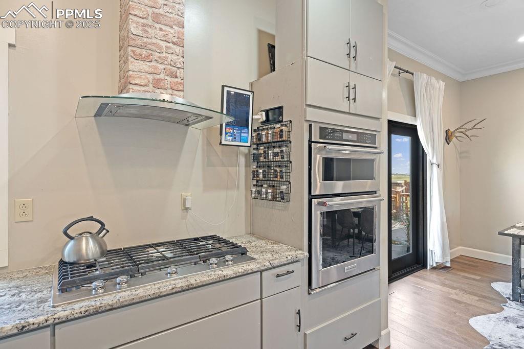 Kitchen featuring wall chimney exhaust hood, white cabinets, stainless steel appliances, crown molding, and light wood finished floors