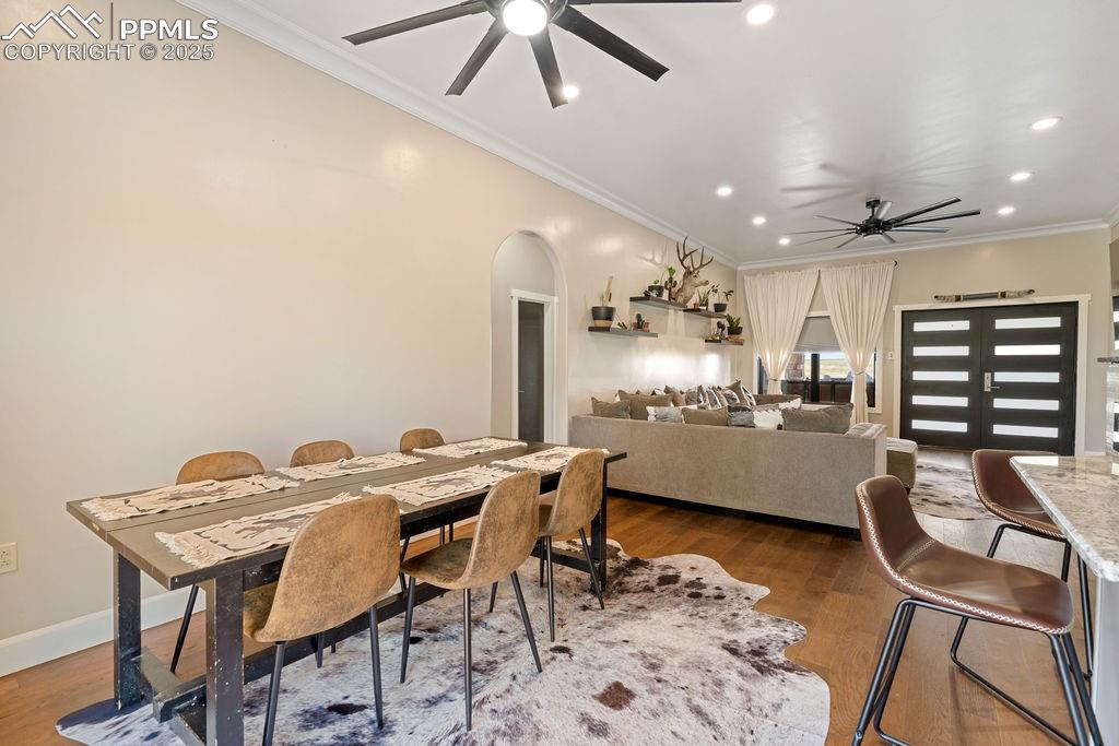 Dining room featuring crown molding, arched walkways, dark wood finished floors, recessed lighting, and a ceiling fan