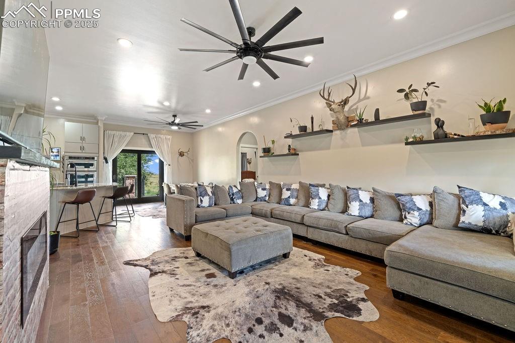 Living room with a glass covered fireplace, ornamental molding, wood-type flooring, recessed lighting, and arched walkways