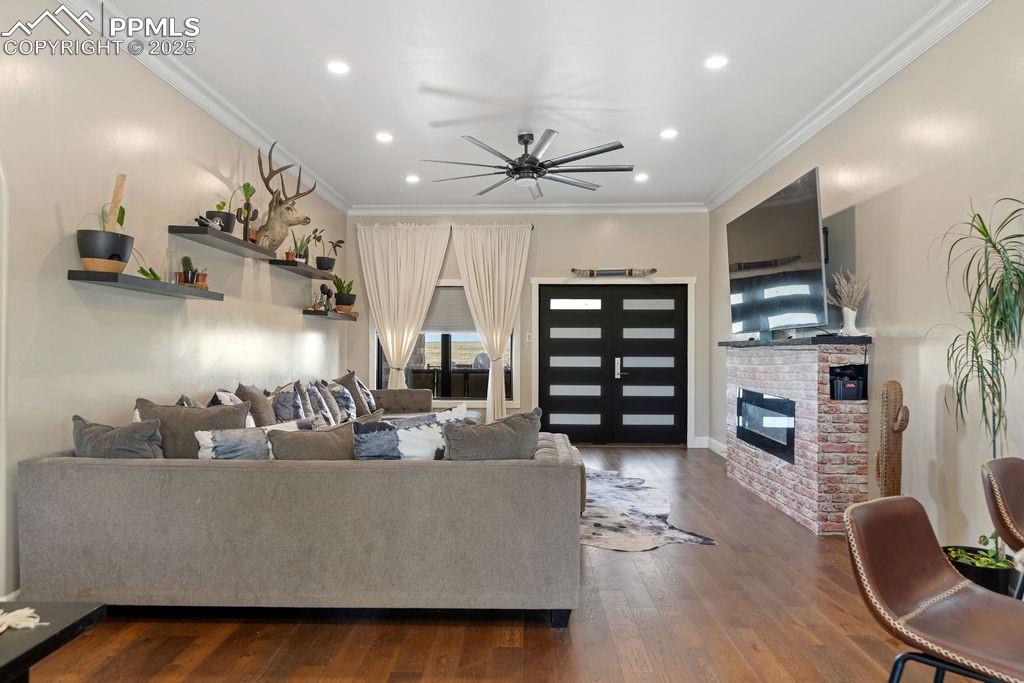 Living room with ornamental molding, recessed lighting, dark wood-type flooring, a ceiling fan, and a brick fireplace