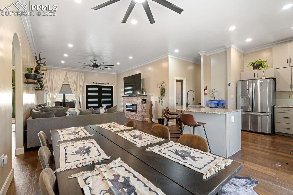 Dining area featuring dark wood-style flooring, ornamental molding, a brick fireplace, recessed lighting, and a ceiling fan