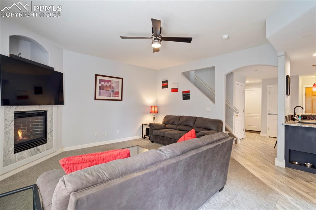 Living area featuring ceiling fan, a fireplace, arched walkways, and light wood finished floors